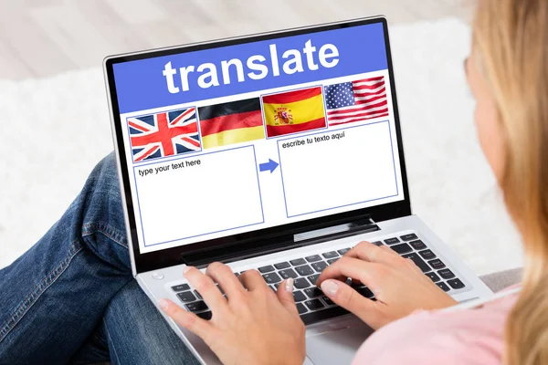 自宅で国旗を持つ言語翻訳アプリケーションを示すラップトップを使用する女性 — ストック写真