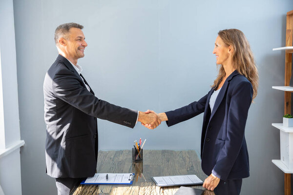 Side View Of Smiling Mature Businessman Shaking Hands With His Colleague In Office