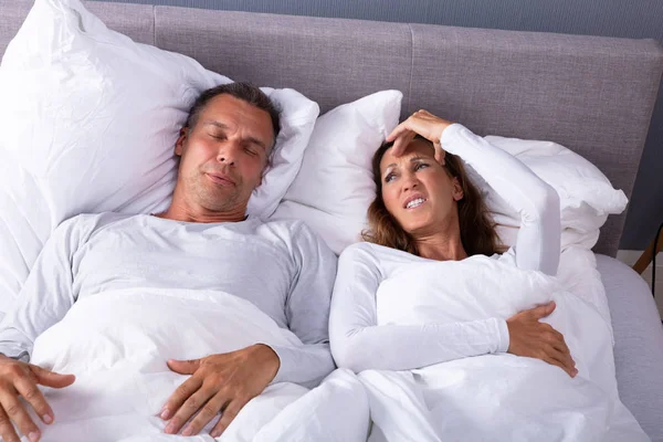 ベッドでいびき夫と横たわっている間に頭痛を持つ成熟した怒っている女性 — ストック写真