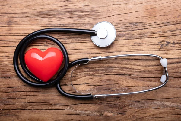 木製デスク上の聴診器を持つ赤い心臓のクローズアップ — ストック写真