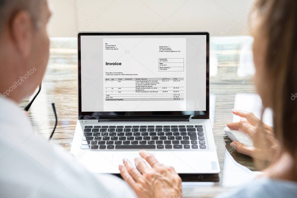 Rear View Of Two Businesspeople Analyzing Invoice On Laptop