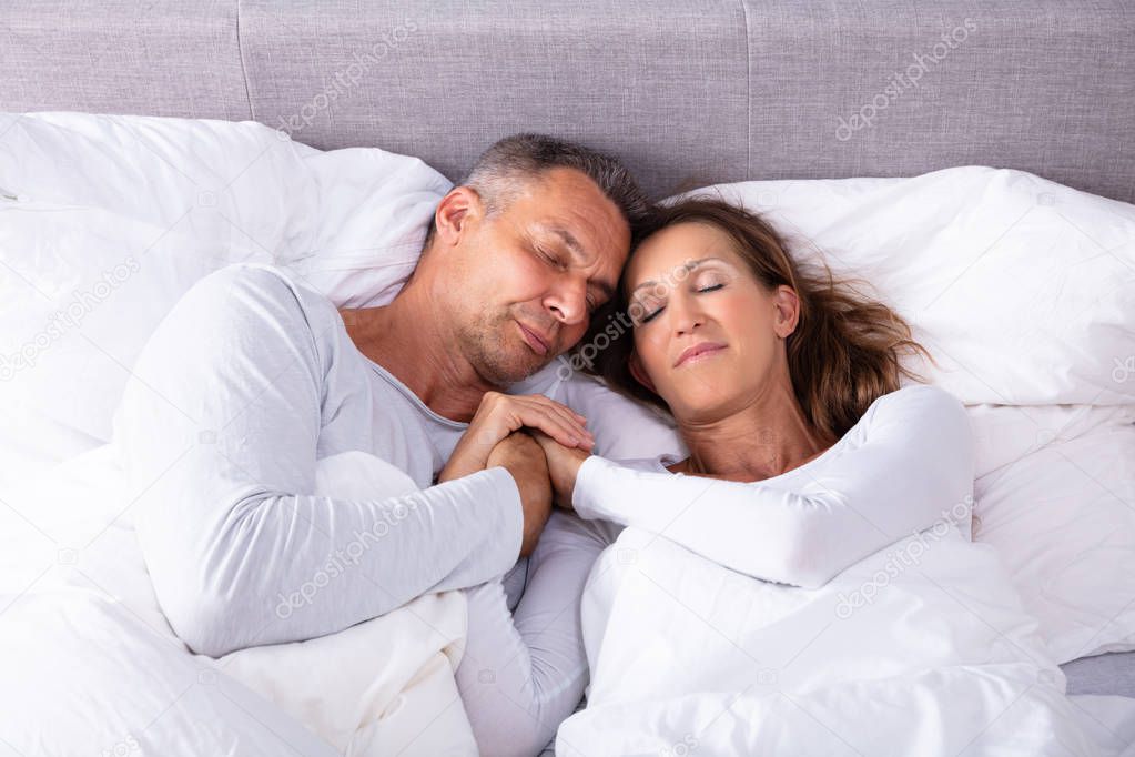 Romantic Mature Couple Sleeping Together On Bed With White Blanket At Home