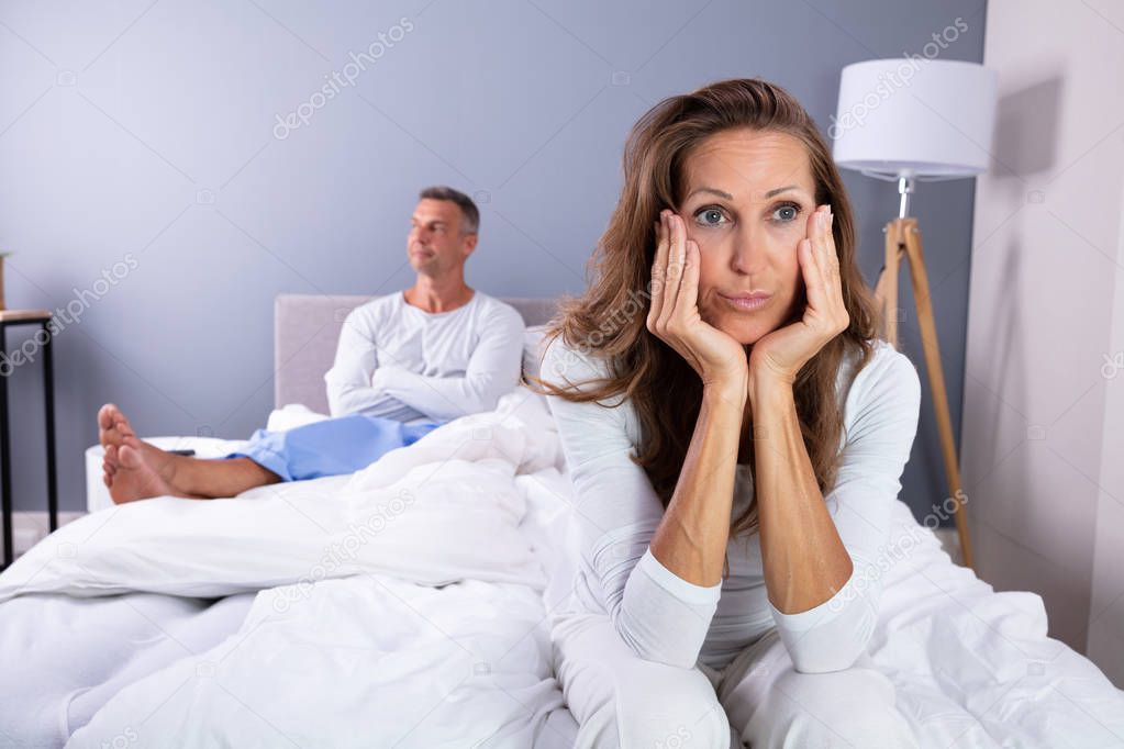 Unhappy Mature Couple Sitting On Bed In Bedroom