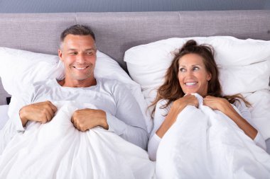 Happy Couple Lying On Bed With White Blanket In Bed Room clipart