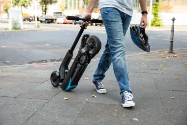 E-scooter taşıyan bir adam işe giderken yolda yürüyor.