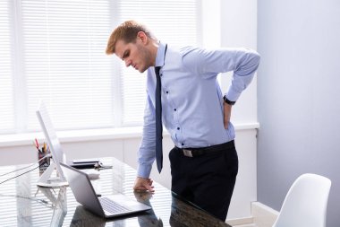 Ofis masasının yanında duran Sırtı Aşağı Ache ile İşadamı