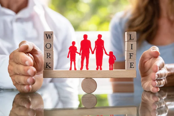 Mid-section Of Couple Protecting Work And Life Balance With Family Figures On Seesaw