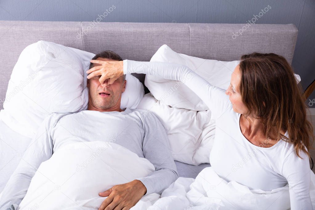 Frustrated Matured Woman Trying To Stop Man's Snoring With Her Finger While Sleeping On Bed