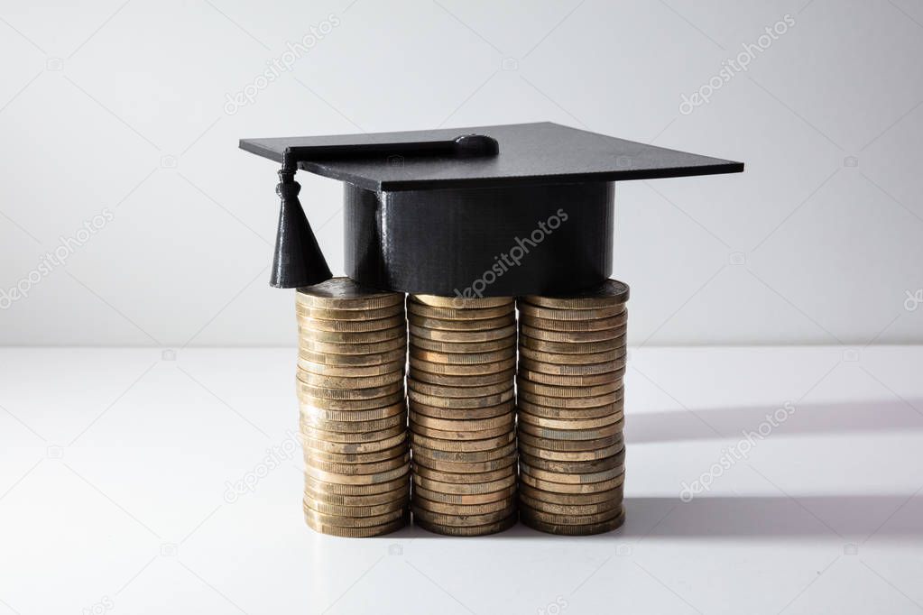 Black Graduation Cap With Tassel Near Stacked Of Coins Isolated Over White Background