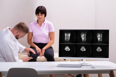 Fizyoterapistin önündeki bilgisayar masası Klinikte oturan kadının diz ağrısını inceliyor.