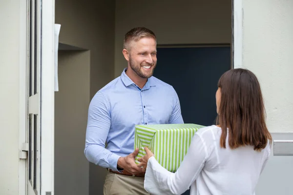 一个男人把礼品盒送给站在门口微笑的邻居的后视镜 — 图库照片