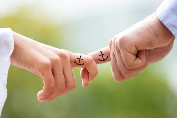 黒のアンカーサインタトゥーで互いの指を保持しているカップルを愛する背景に — ストック写真