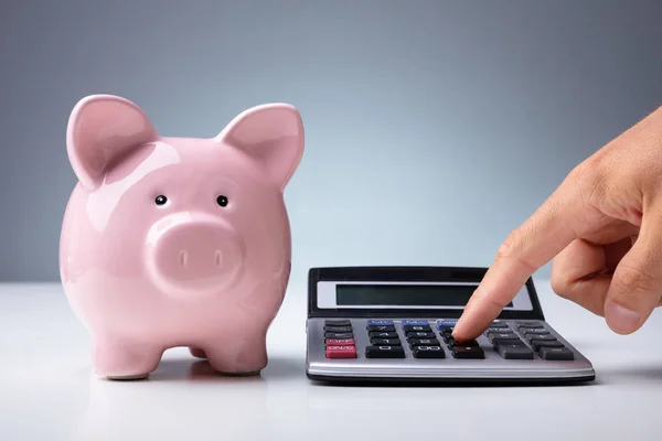 Крупный План Человека Рассчитывающего Помощью Калькулятора Возле Банка Розовая Свинья — стоковое фото