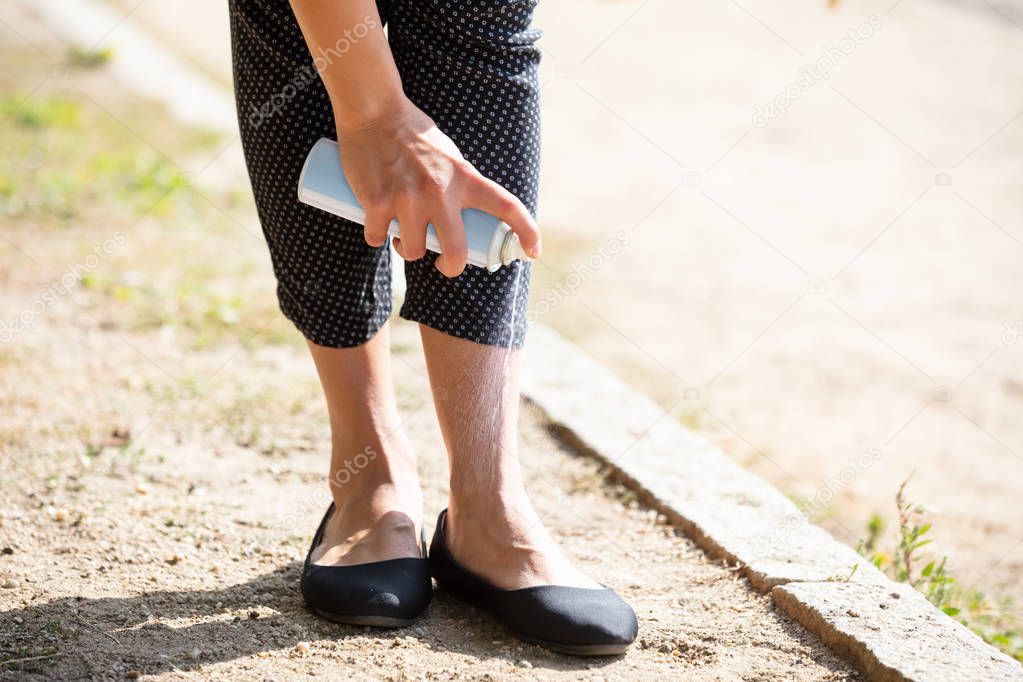 Low Section Of Woman Standing Outdoor Spraying Anti Insect Deet Spray On Her Foot