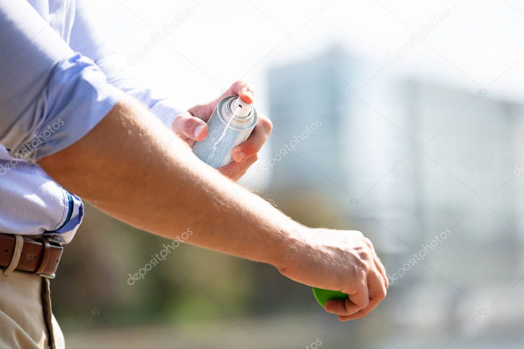 Man Spraying Anti Insect Deet Spray On Skin Over His Arm Outdoors