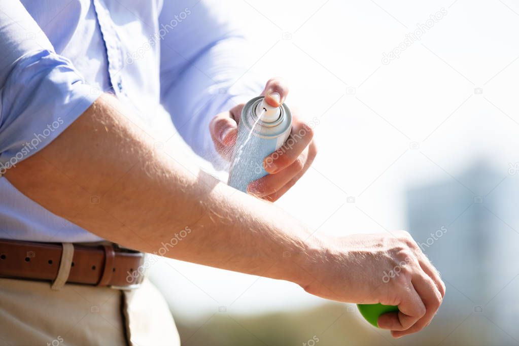 Man Spraying Anti Insect Deet Spray On Skin Over His Arm Outdoors