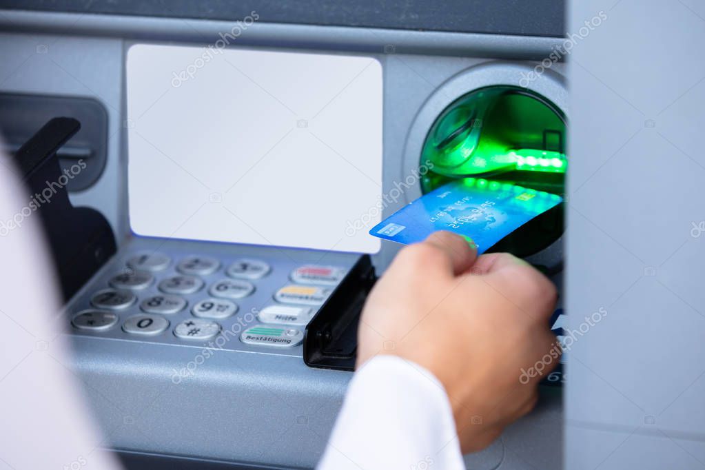 Close-up Of A Person's Hand Insert Card Into ATM Machine Slot To Withdraw Money