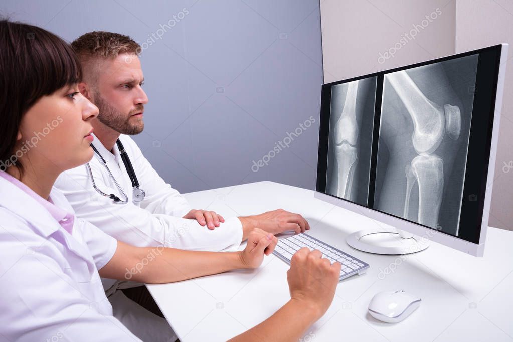 Doctors Examining Knee X-ray On Computer In Clinic