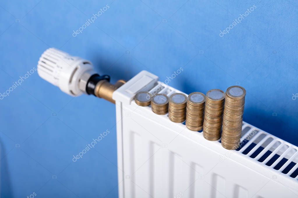 Stacked Of Coins Arrange In Row On Radiator In Front Of Blue Wall