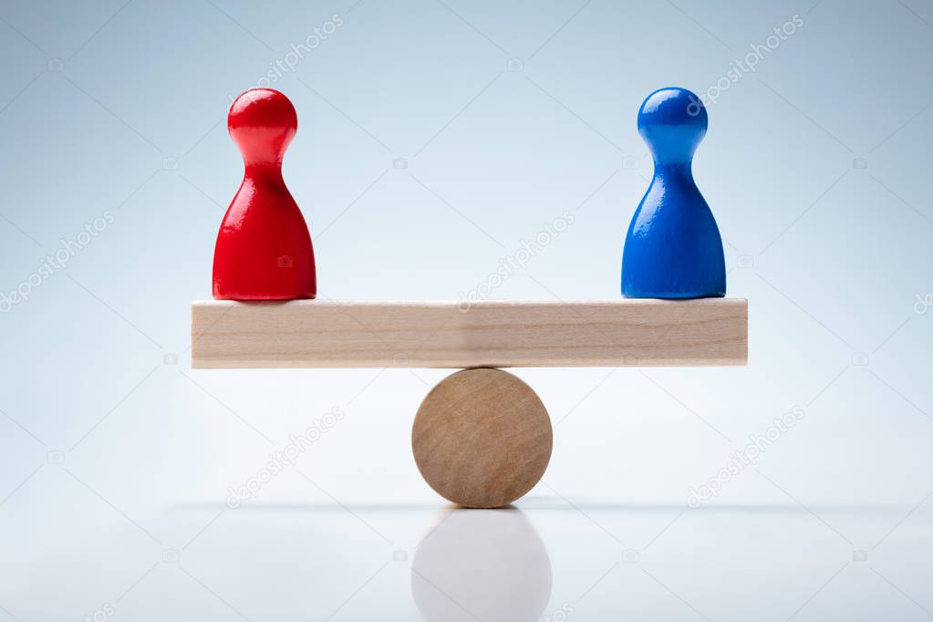 Red And Blue Pawn Figures On Wooden Seesaw Over Reflective Desk
