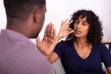 Erkek ve kadın işaret diliyle iletişim kuruyor. Koltukta oturuyor.