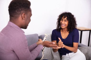 Erkek ve kadın işaret diliyle iletişim kuruyor. Koltukta oturuyor.