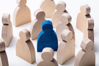Close-up Of A Blue Human Figure Surrounded With Wooden Figures Over White Desk clipart