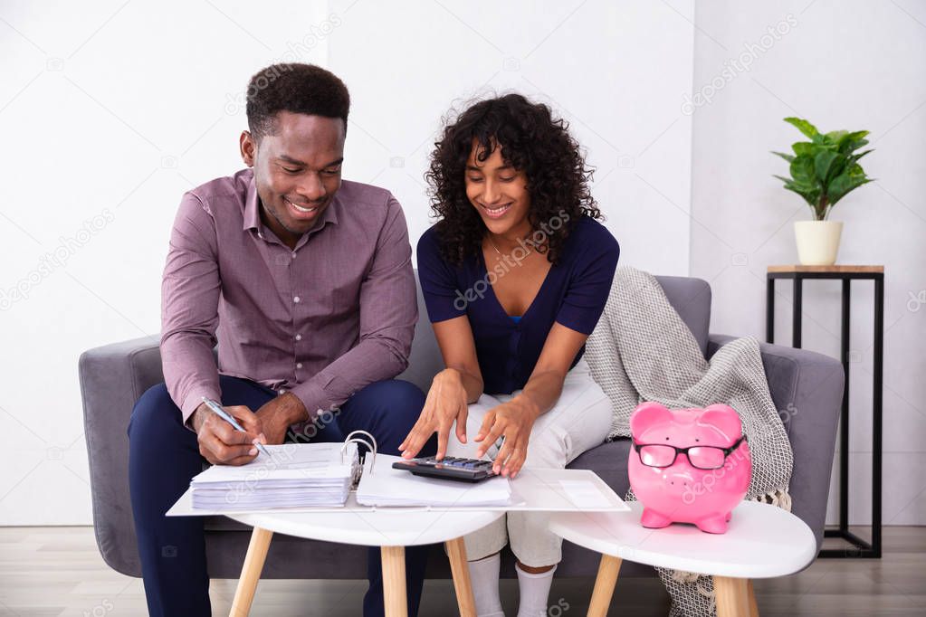 Young Couple Sitting On Sofa Calculating Invoices At Home 