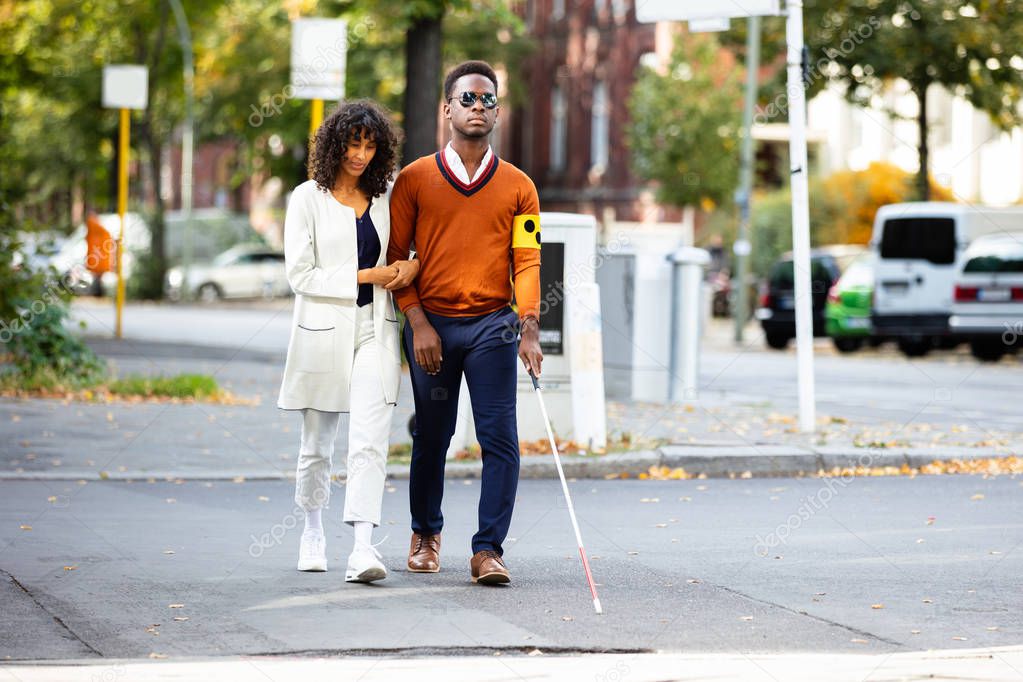 Young Woman Assisting Blind Man On Street