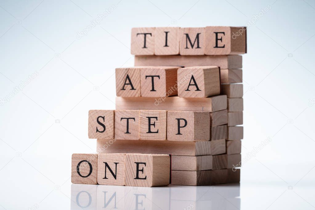 One Step At A Time Message On Wooden Blocks Over Reflective Desk