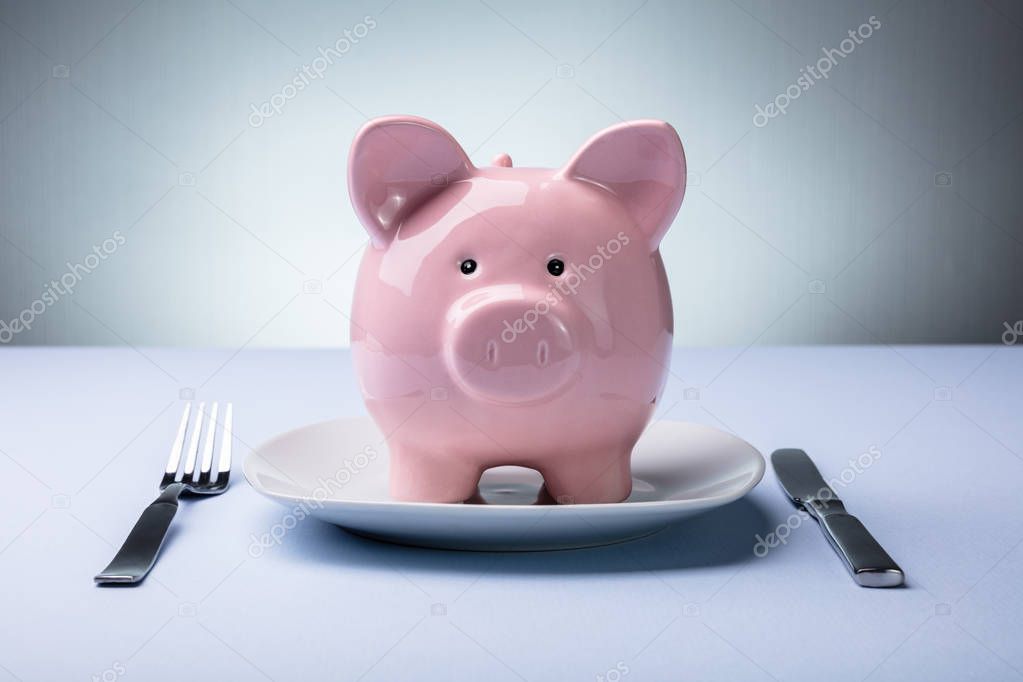 Elevated View Of Pink Piggy Bank On The White Plate With Fork And Knife