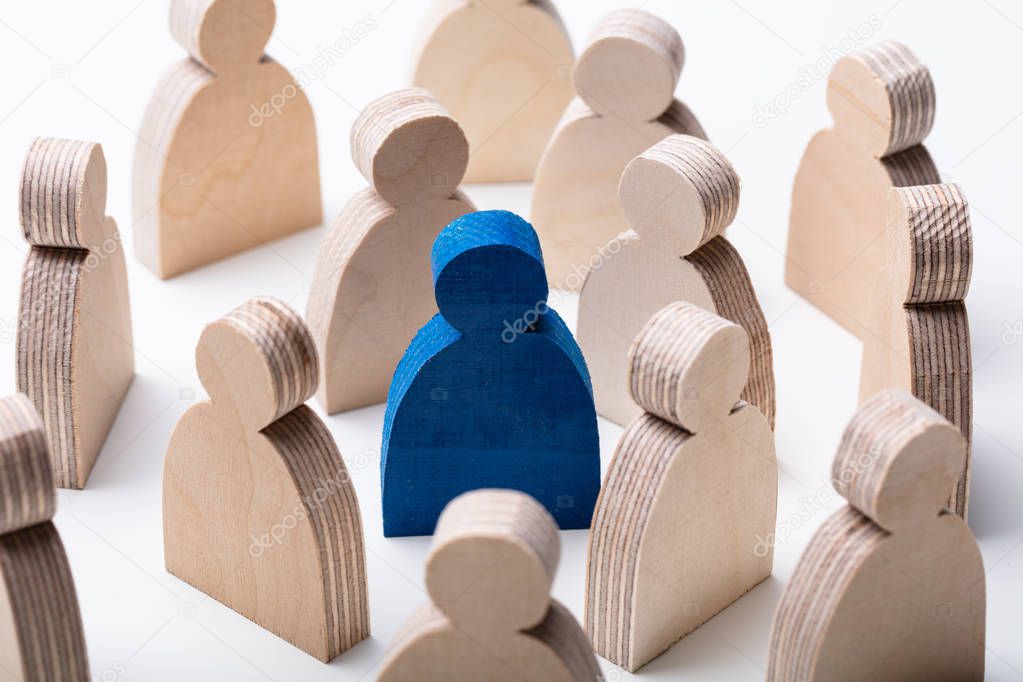 Close-up Of A Blue Human Figure Surrounded With Wooden Figures Over White Desk