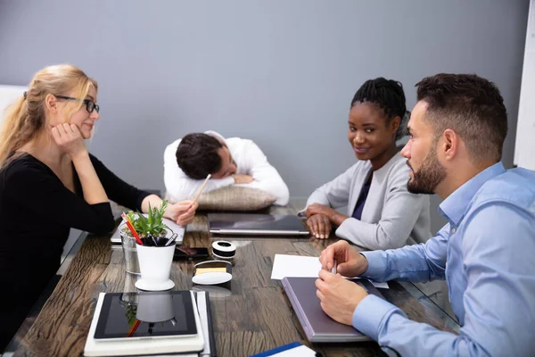 Müder Geschäftsmann Schläft Auf Schreibtisch Während Seine Kollegen Besprechung Diskutieren — Stockfoto