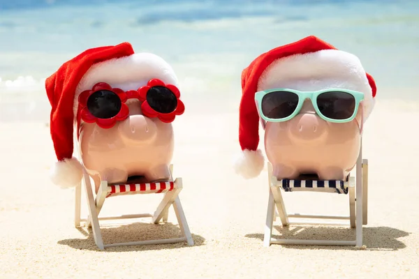 Nahaufnahme Von Zwei Rosa Sparschweinen Mit Weihnachtsmützen Auf Liegestuhl Strand — Stockfoto