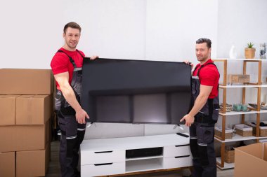 Üniformalı iki profesyonel nakliyeci oturma odasına Lcd Televizyonu boşaltıyor.