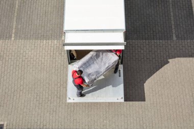 An Elevated View Of Male Mover Unloading The Furniture From Truck On Cobblestone Pavement clipart