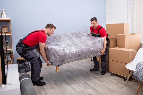 Portrait Two Young Happy Male Movers Carrying Wrapped Sofa New — Stok Foto