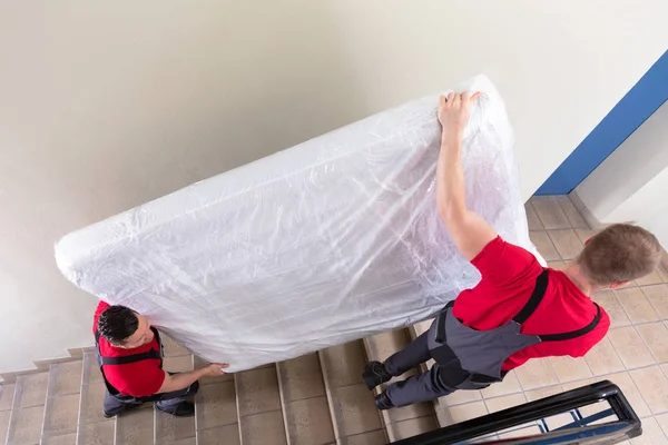 Two Young Male Movers Uniform Carrying Wrapped Mattress While Moving — Stock Photo, Image