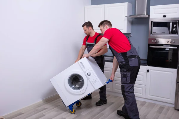 Dos Jóvenes Hombres Profesionales Mueven Uniforme Colocando Lavadora Moderna Cocina —  Fotos de Stock