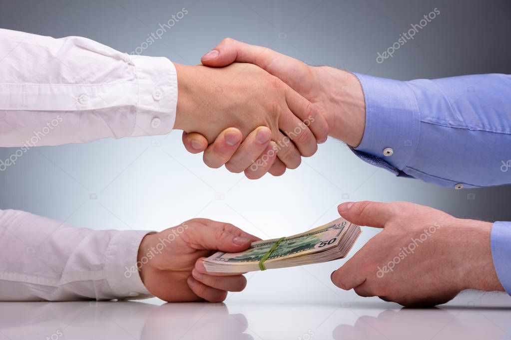 Close-up Of Businessmen Sealing The Deal With Handshake And Receiving A Bribe Money