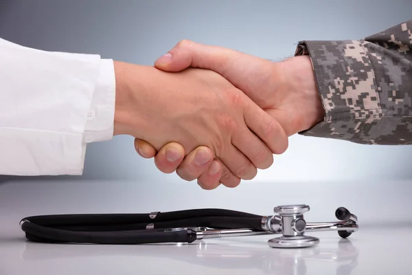 医者と軍の男は白いテーブルの上に聴診器を握手 — ストック写真