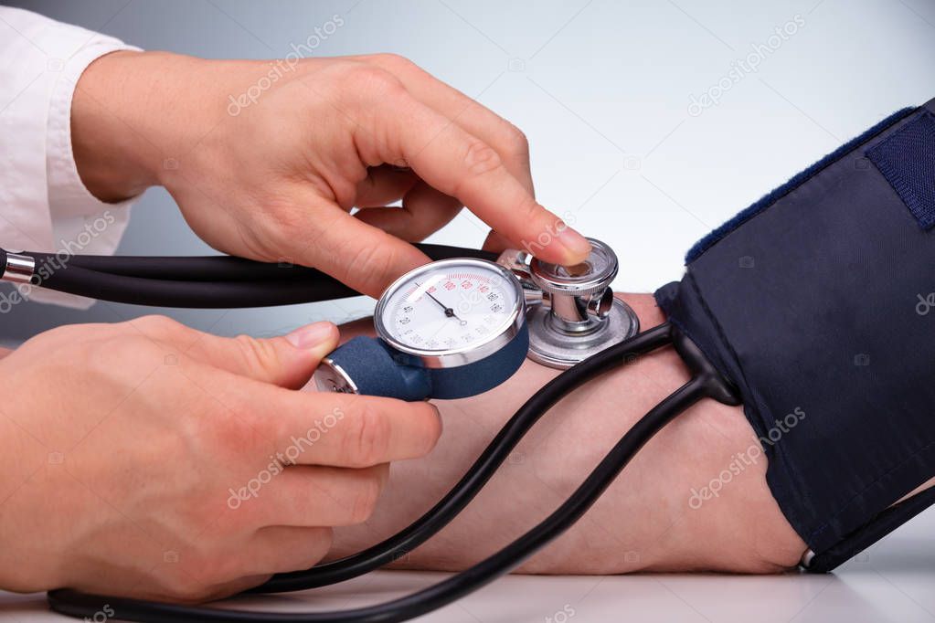 Close-up Of Doctor Checking Blood Pressure Of The Male Patient On Table Against Gray Background