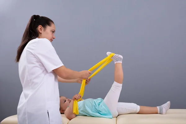 Dívka Protahování Noha Žlutým Elastickým Pruhem Instruktáž Žena Fyzioterapeut Klinice — Stock fotografie