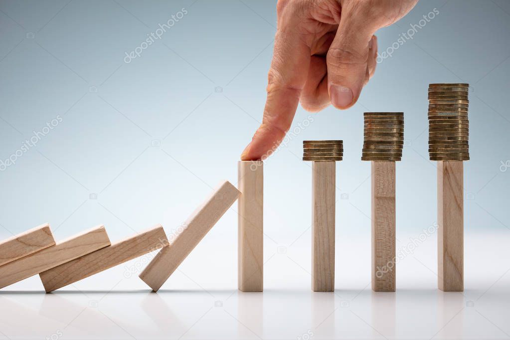 Cropped Image Of Businessman's Hand Protecting Coins From Falling While Playing Domino On Table