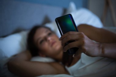 Geceleri yatakta cep telefonlu bir kadın.