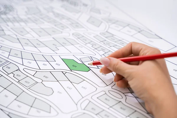 Close-up Of Human Hand Holding Pencil Over Paper Cadastre Map