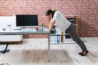 Ofis masasında şınav çeken genç bir iş kadınının yan görüntüsü