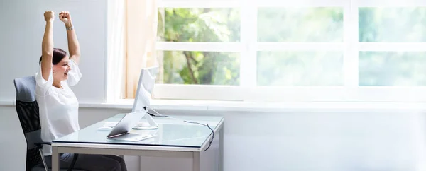 Happy Woman At Computer Desk With Hands Raised