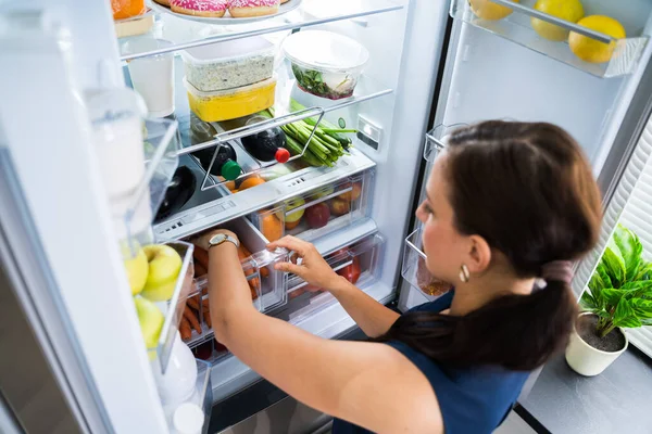 台所で冷蔵庫の中に食べ物を探している女性 — ストック写真