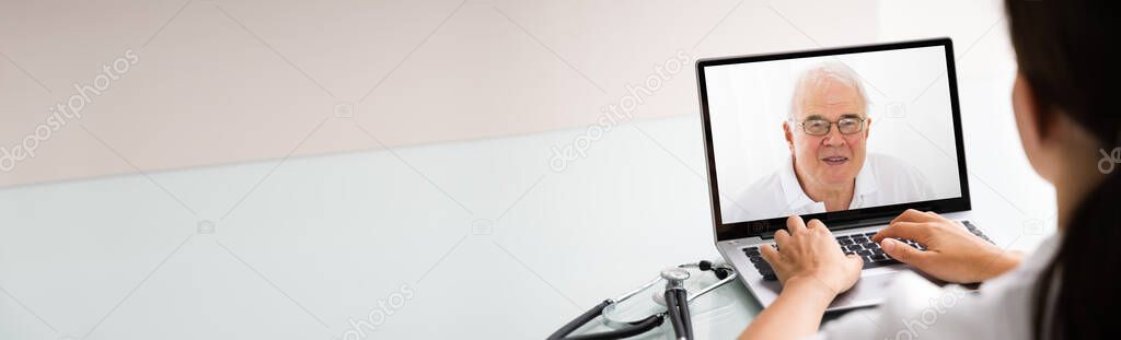Doctor Talking To Male Patient Through Video Chat On Laptop At Desk